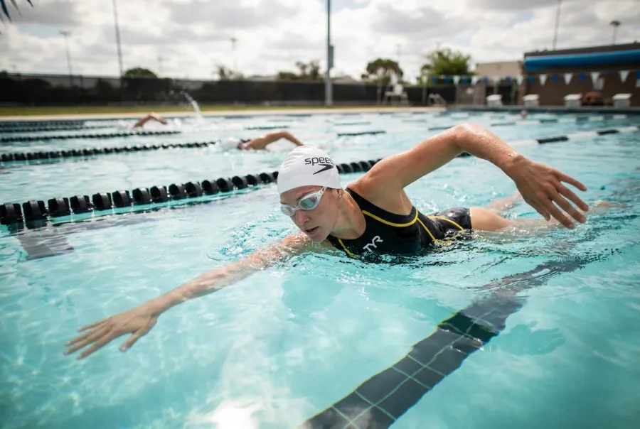 Triathlete swimming easy aerobic technique-focused laps in a pool during base training wearing TYR goggles and a Speedo swim cap