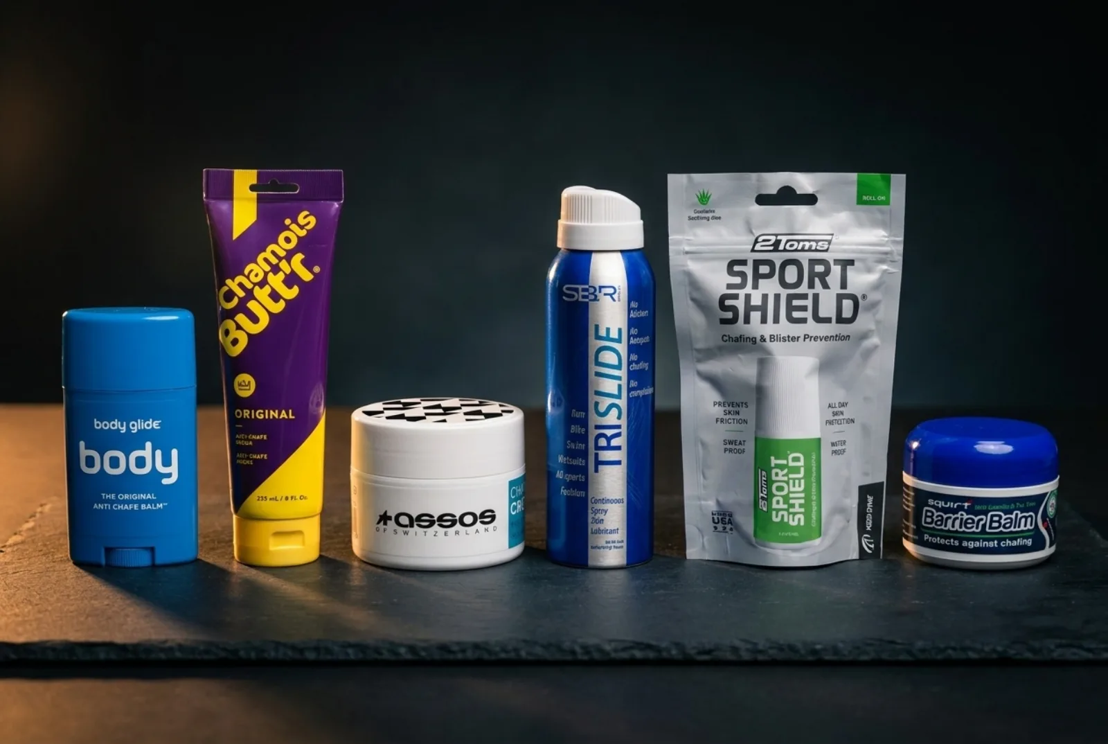 Flat lay of triathlon anti-chafe balms and chamois creams including Body Glide, Chamois Butt'r, and Assos on a bike trainer mat