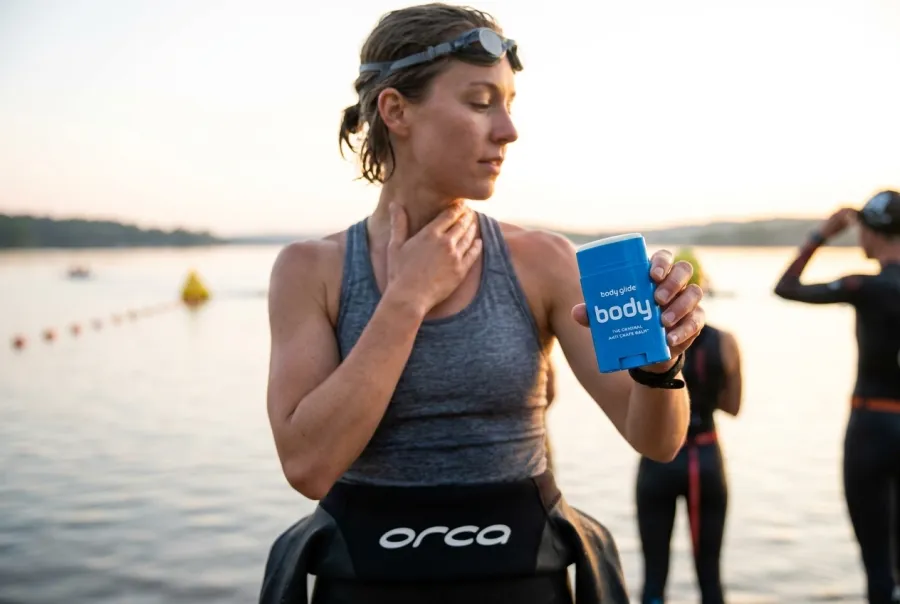 Female triathlete applying anti-chafe balm to her underarm and wetsuit neckline before an open-water swim start