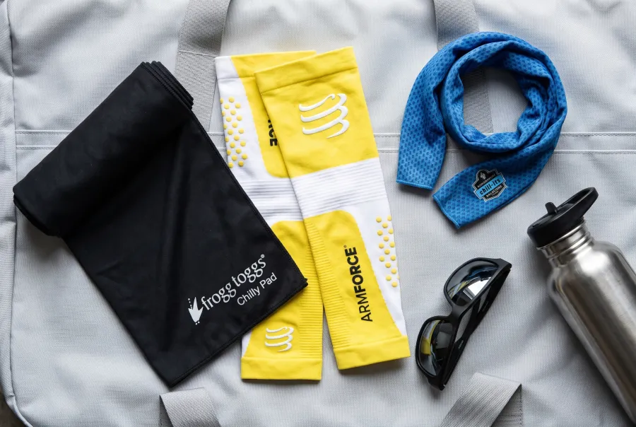 Frogg Toggs Chilly Pad cooling towel, Compressport ArmForce arm sleeves, and an Ergodyne Chill-Its cooling neck wrap laid out together on a training bag