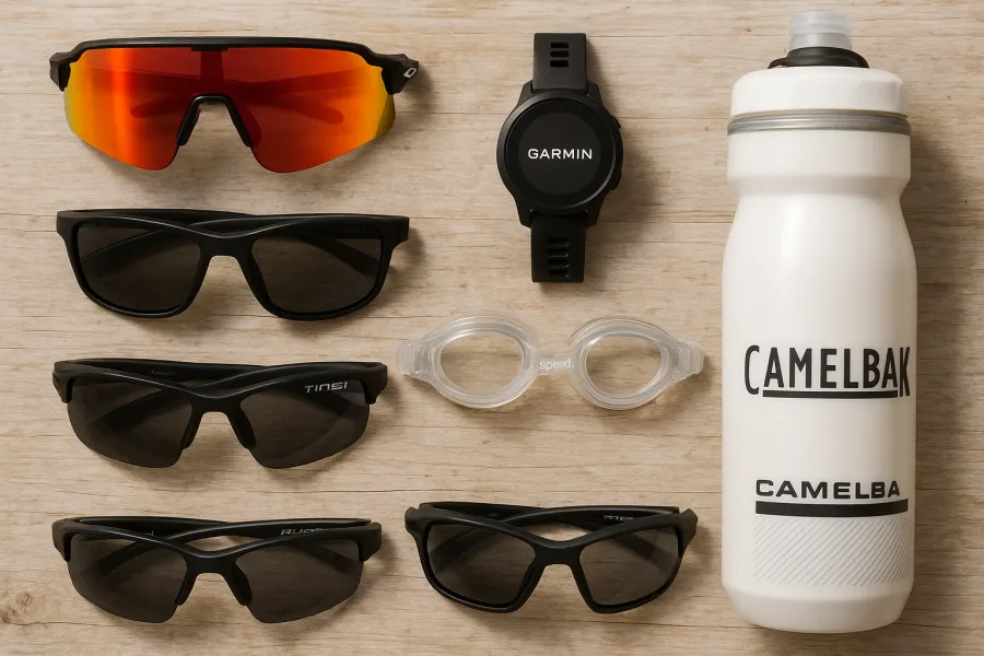 Flat-lay of four pairs of sport sunglasses next to a water bottle, swim cap, and goggles