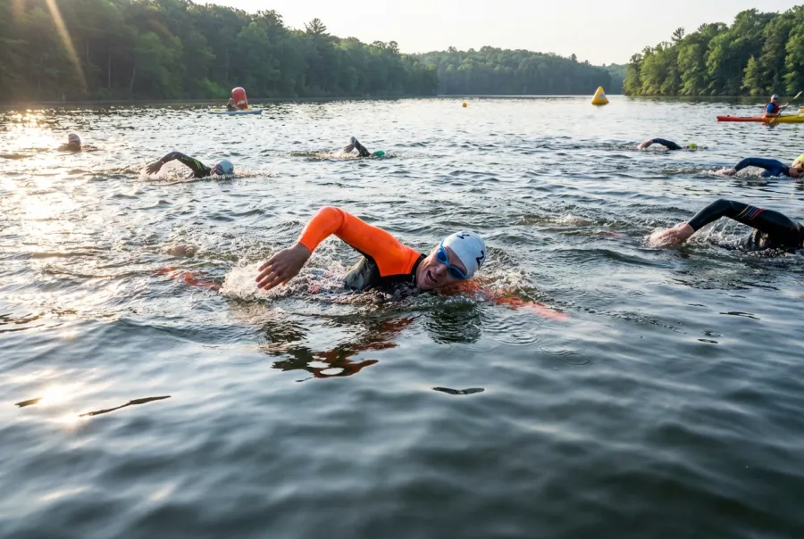 Beginner triathlete swimming in open water during a race wearing a bright orange wetsuit