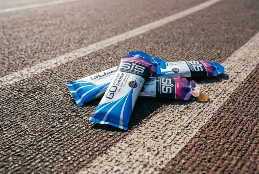 SiS GO Isotonic Energy Gel packets on running track — photorealistic product shot