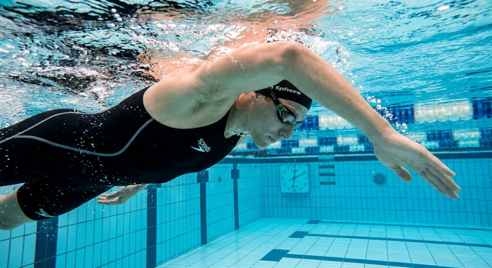 Triathlete in lane pool mid-freestyle stroke showing high-elbow catch technique