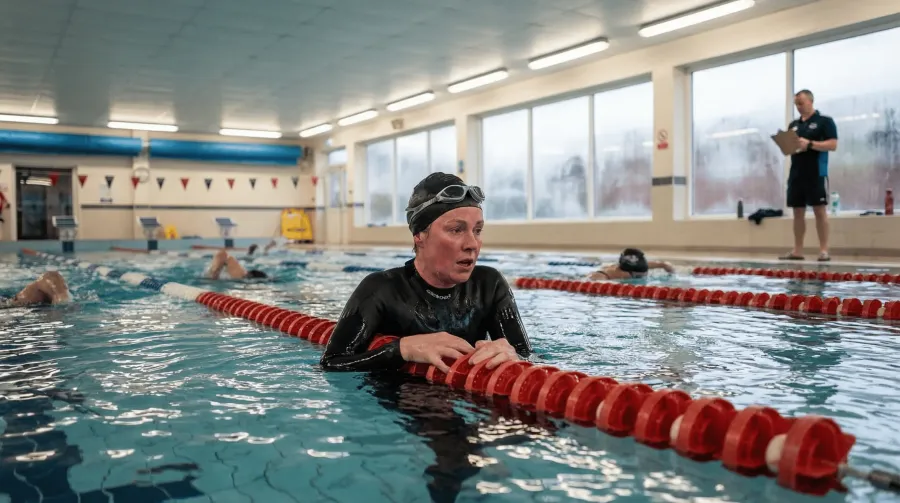 Beginner swimmer in a wetsuit gripping the lane rope at a public pool, catching breath after a difficult swim set