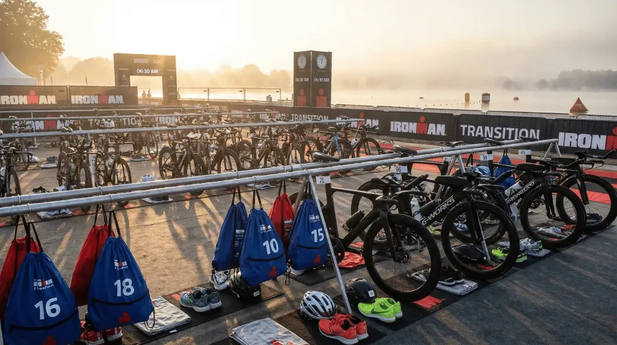 Ironman transition zone at dawn with rows of carbon fiber bikes racked and transition bags laid out