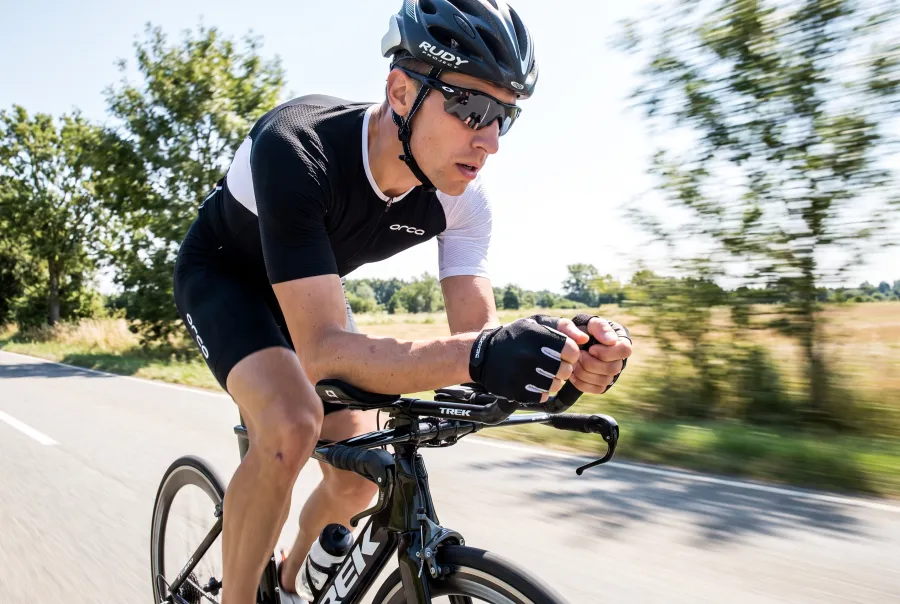 A triathlete riding a road bike fitted with clip-on aero bars on a sunny open road, in an aggressive aero position
