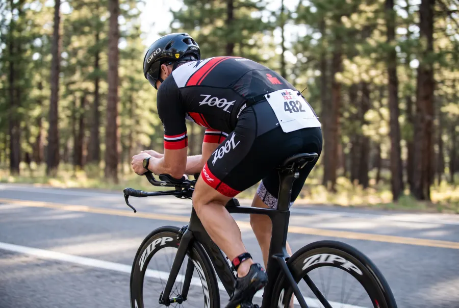 A triathlete riding a time trial bike through pine forest on the flat IRONMAN Florida bike course near Panama City Beach