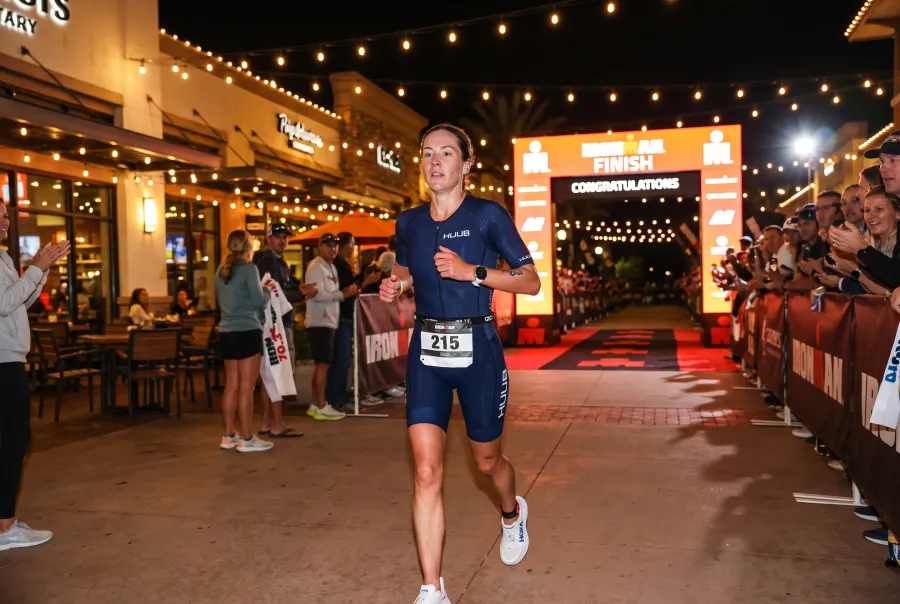 A triathlete running past cheering spectators near the Pier Park finish line at IRONMAN Florida in Panama City Beach at night