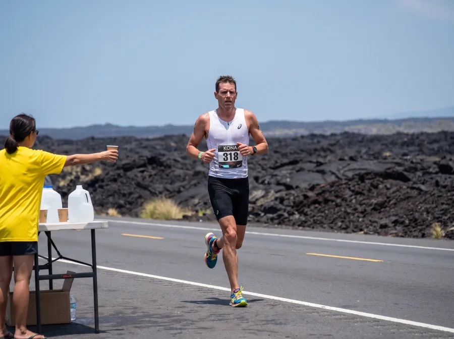 A triathlete running along the lava fields of the Queen Kaahumanu Highway near Kona in extreme heat with heat shimmer visible on the road