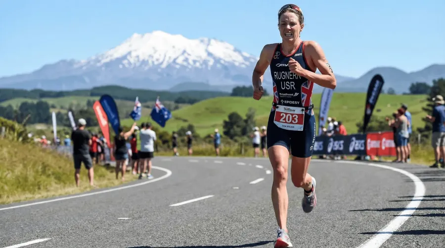 Elite professional female triathlete running at full race pace on a sun-drenched New Zealand road with volcanic peaks
