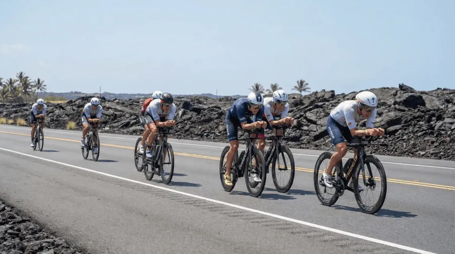 Elite triathletes in aero position on TT bikes racing along the Queen K Highway with Hawaiian lava fields on both sides