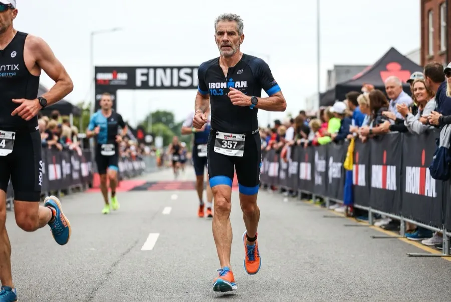 Masters triathlete in his 50s running the run leg of a triathlon, Hoka shoes and Garmin watch visible