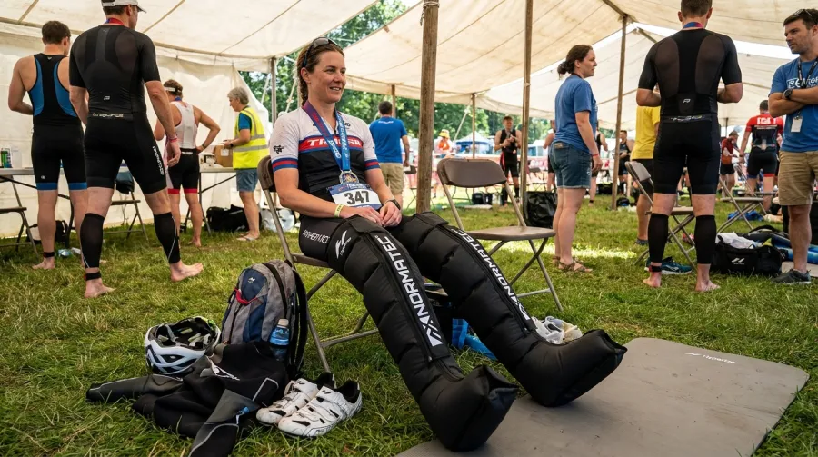 Triathlete wearing Normatec compression leg sleeves during post-race recovery in athlete area