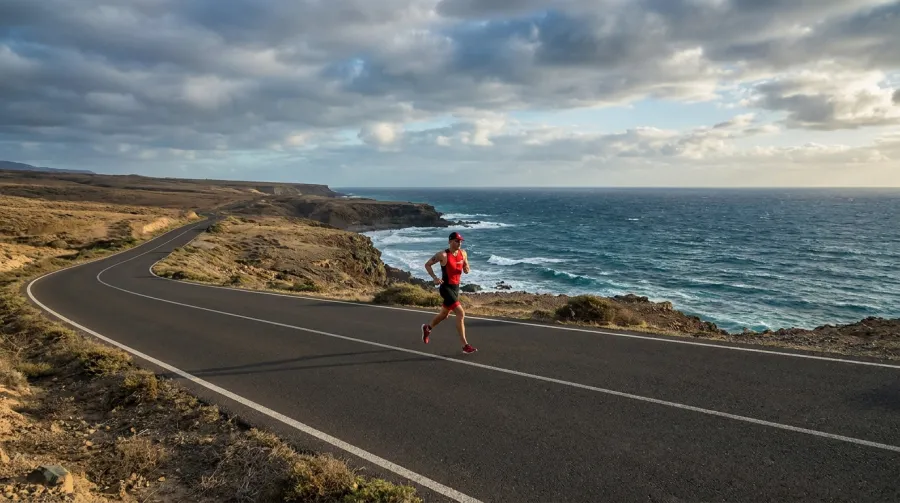 Triathlete running strongly on a flat coastal road under a bright sky