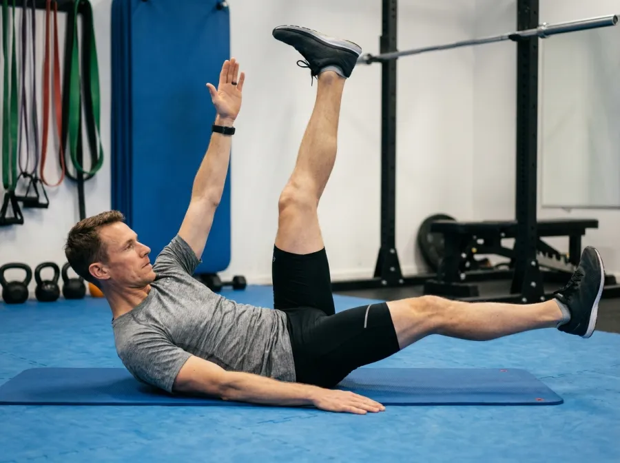 Lean triathlete performing dead bug core exercise on a gym mat