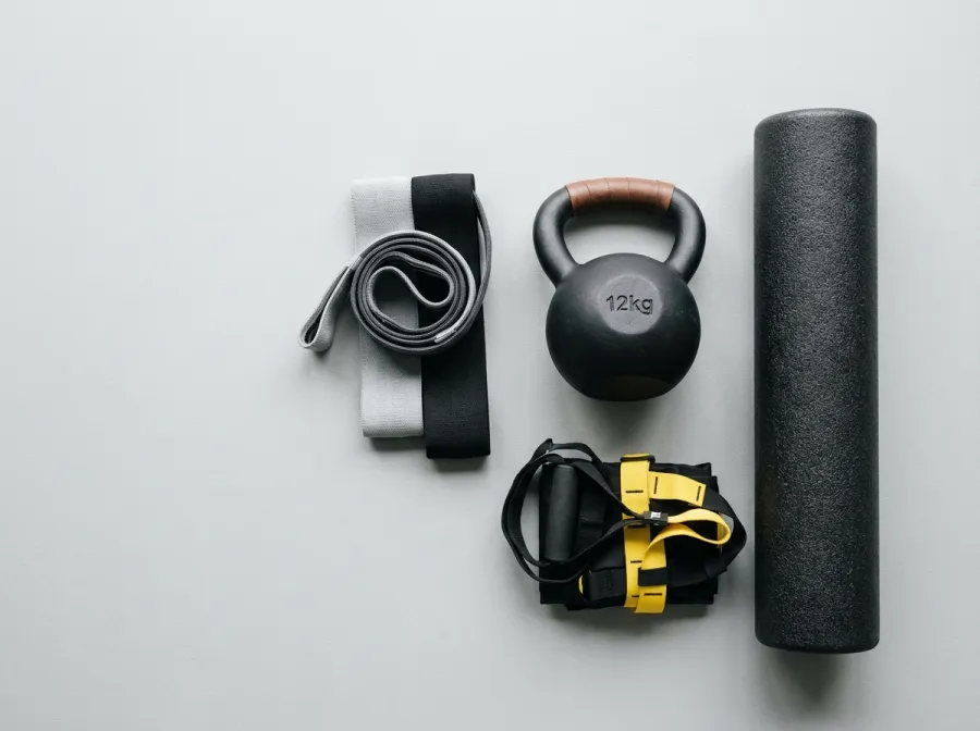 Flat-lay of triathlon strength training equipment: kettlebell, resistance bands, foam roller, and TRX straps on gym floor