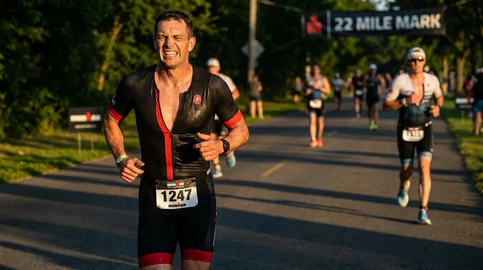Triathlete grimacing and pushing through the run leg of an IRONMAN race, visibly suffering at mile 22