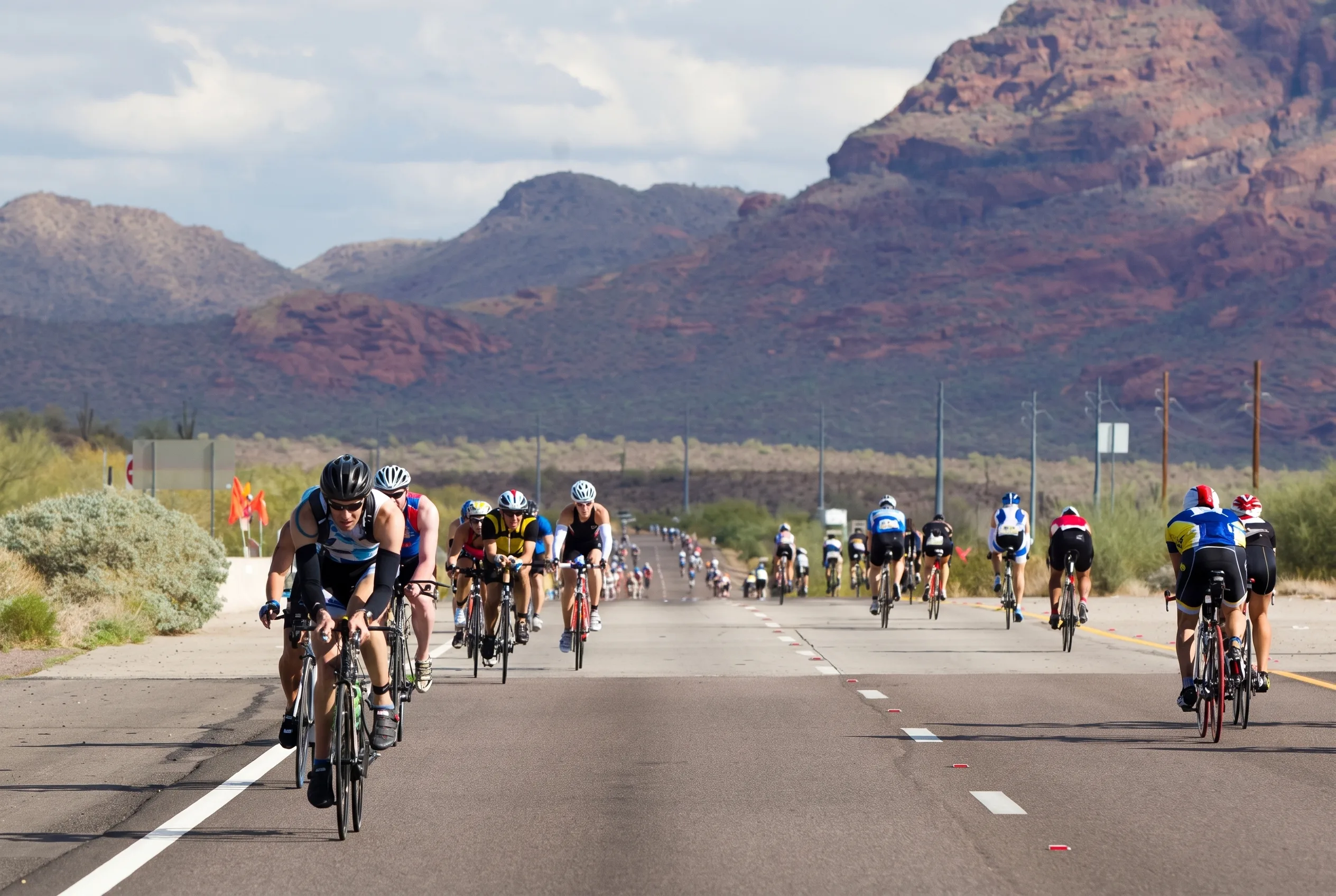 Triathletes riding time trial bikes on the Beeline Highway during the Ironman Arizona bike course with desert terrain in the background