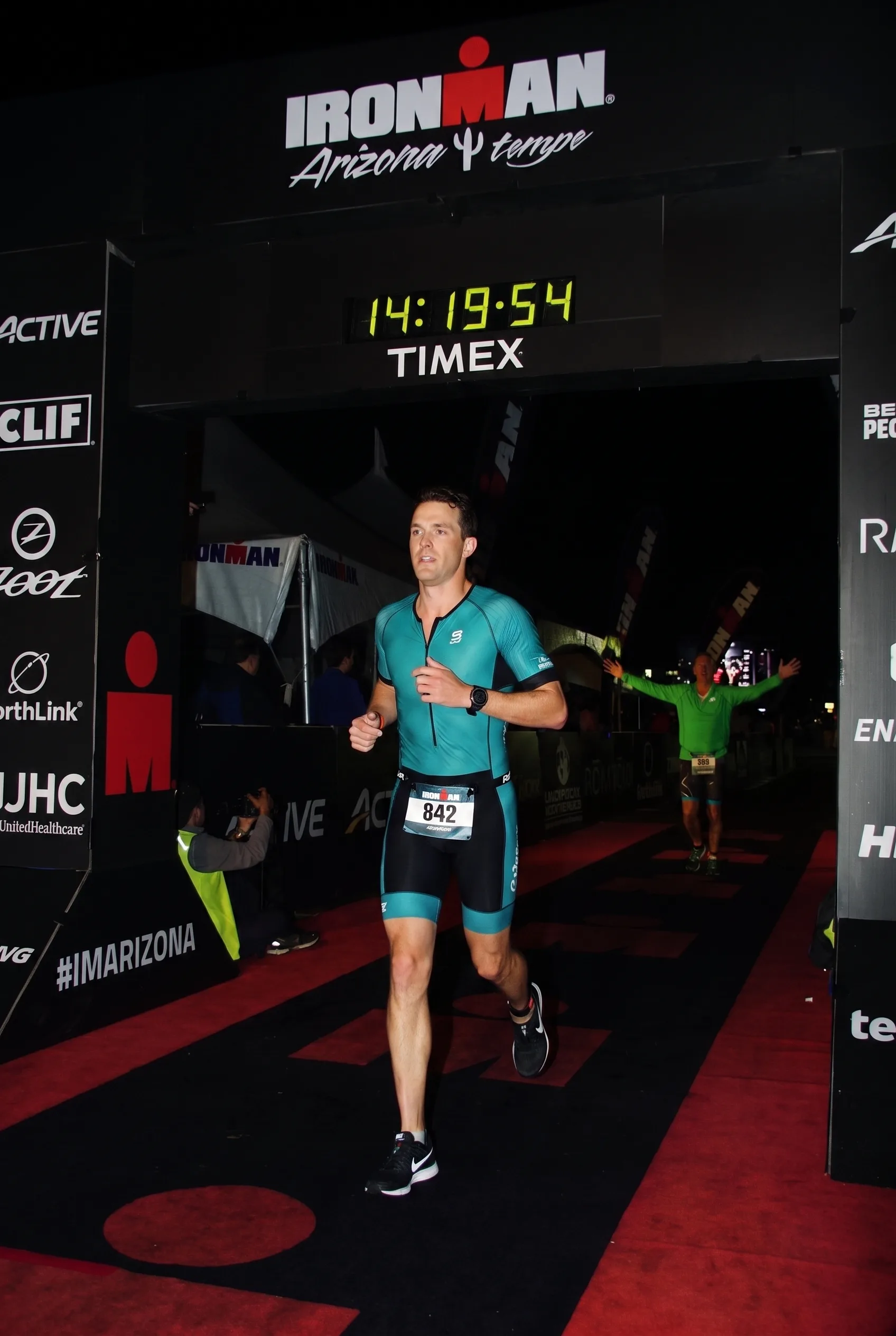 A triathlete running the final stretch of the Ironman Arizona run course at night near the lit finish line